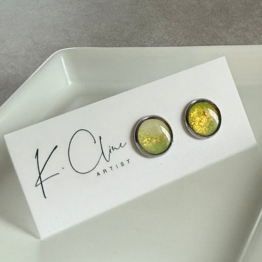 Pair of green earrings on a white box with 'K. Cline Artist' branding on a gray surface.